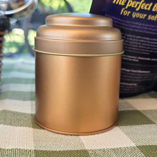 A metallic bronze cylindrical tin on a green and white checkered tablecloth, with a wicker basket and a dark blue bag in the background.